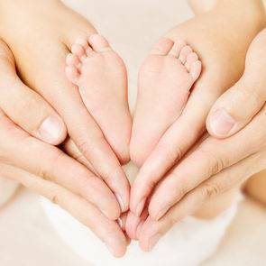 Newborn baby feet parents holding in hands. Love simbol as heart sign.